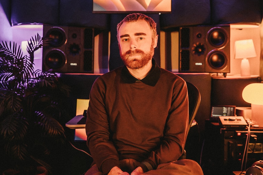 A white male adult with short hair and a beard sitting in a music studio