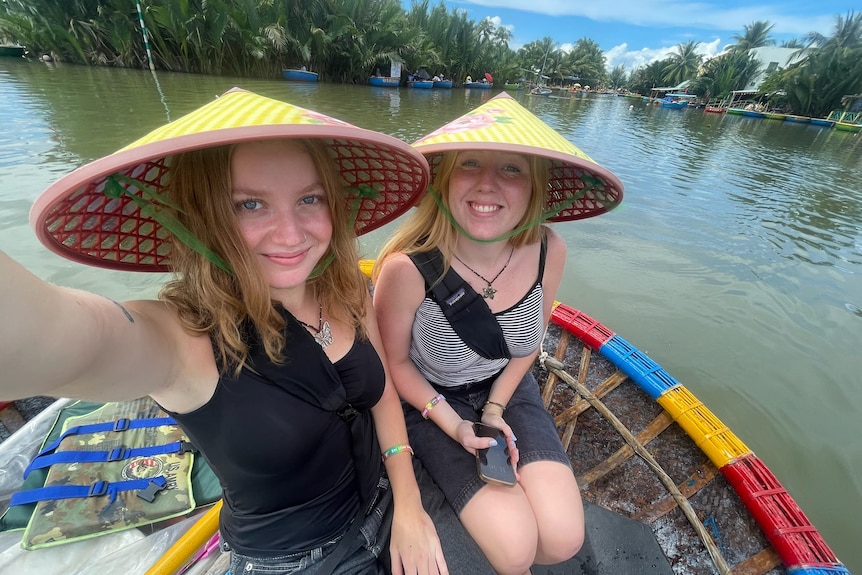 Two girls take a selfie while wearing hats on a boat.