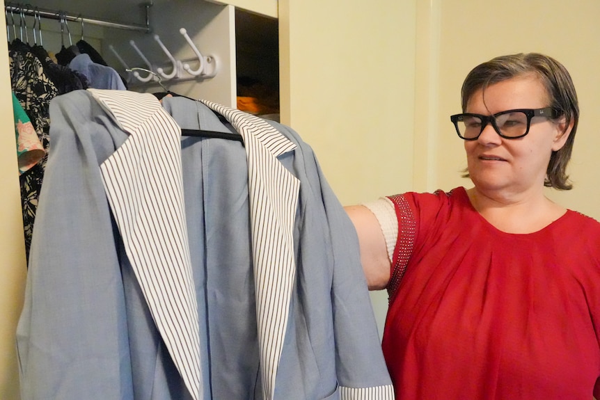 Blind woman wearing Meta Glasses holds up and looks at jacket in her bedroom.