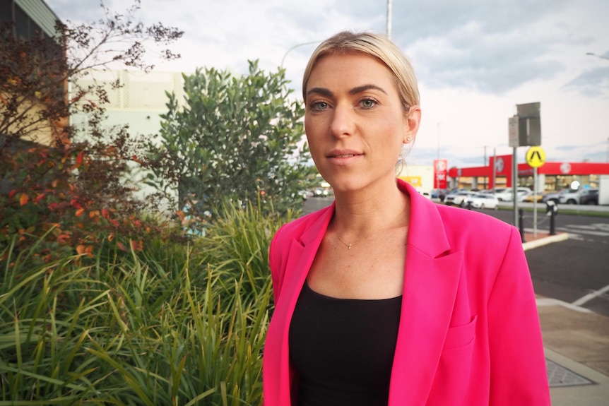 Woman in bright blazer stares into camera with a neutral expression.