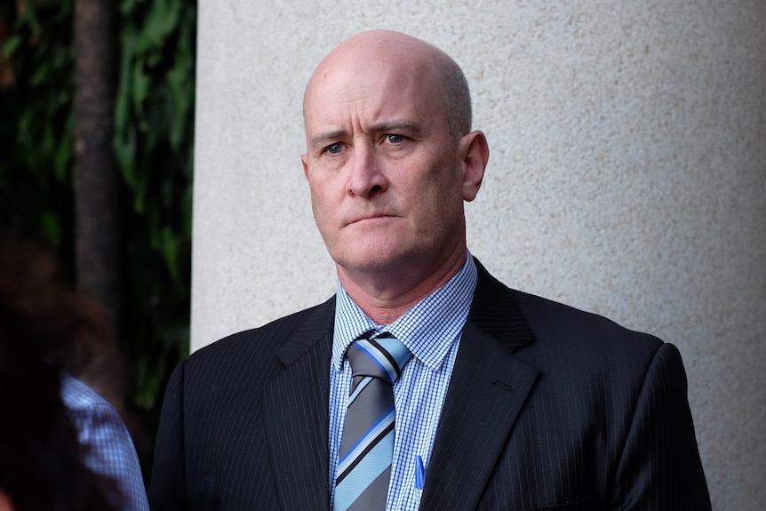 A man in a suit with a bald head looks serious.