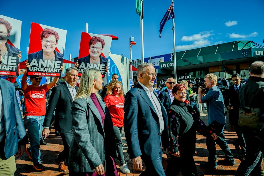 Anthony Albanese, wearing a suit, marches down a street in front of a crowd carrying election propaganda.