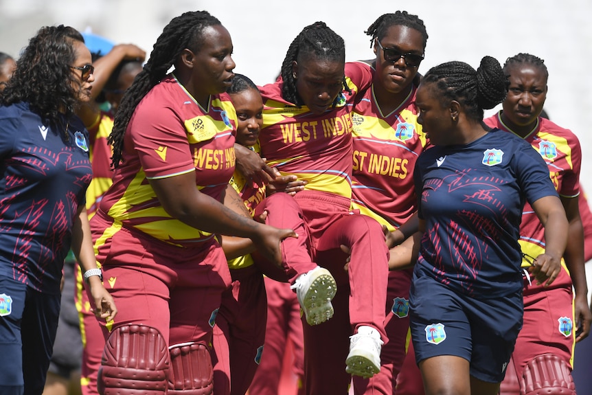 A cricketer is carried off the field by teammates.