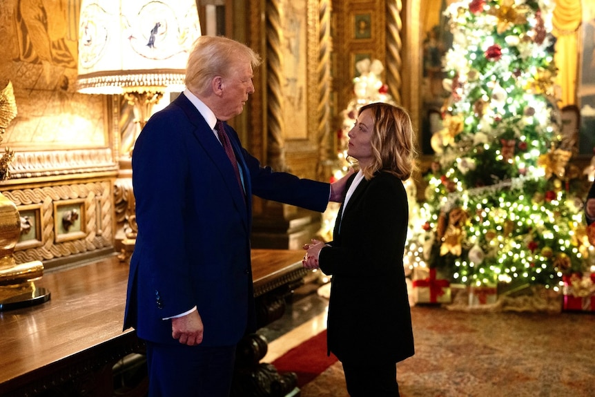 A man and a woman speaking in an opulent room. The man has his hand on the woman's shoulder.