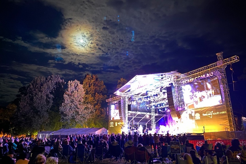 Stage with bright purple lights and a crowd of people at the outdoor festival.