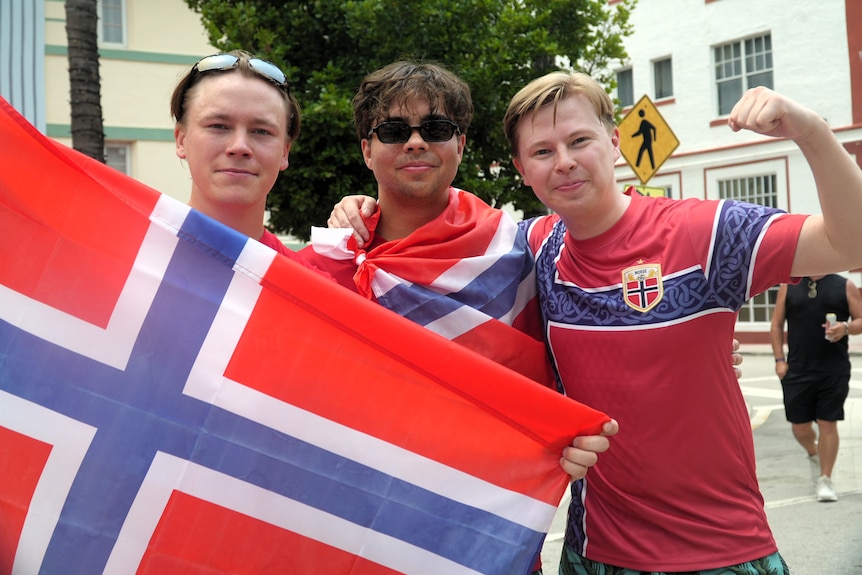 Three Norwegian men smile and hold a Norway flag.