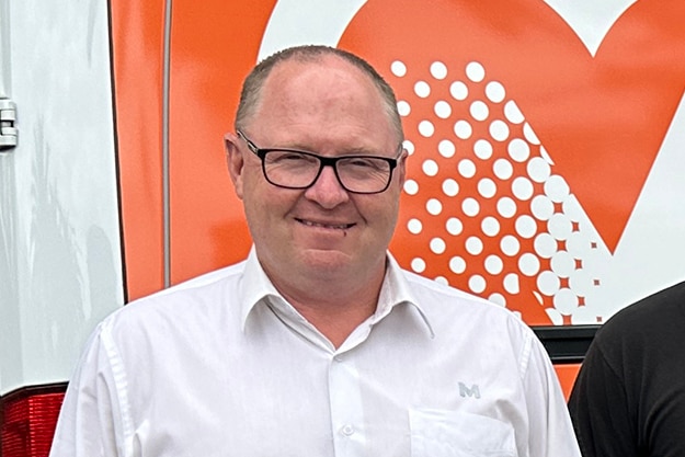 Terry Welch wearing glasses and standing in front of an orange background