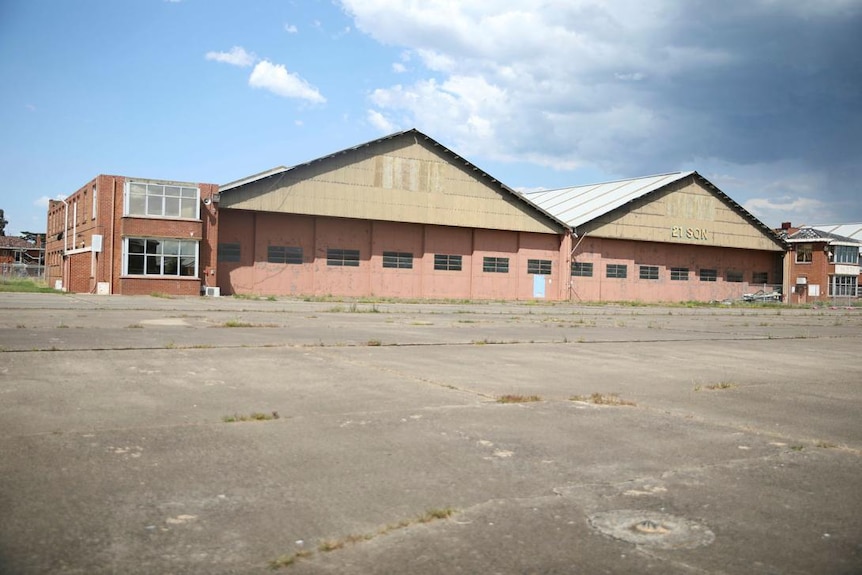 A double storey orange brick building with two peaked roofs beside a large concrete ground.