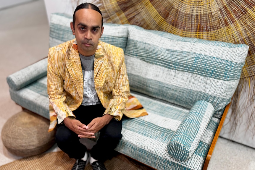 A man sits on a green and white striped lounge chair.