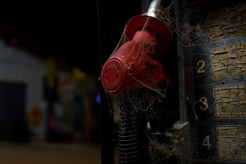 An eerie close-up photo of an old fuel pump's handle, which is covered in dust and cobwebs, taken at night time.