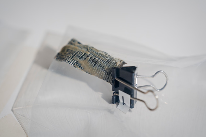 A close up shot of a piece of duct tape held with a black bull clip inside a clear evidence bag on a white table.