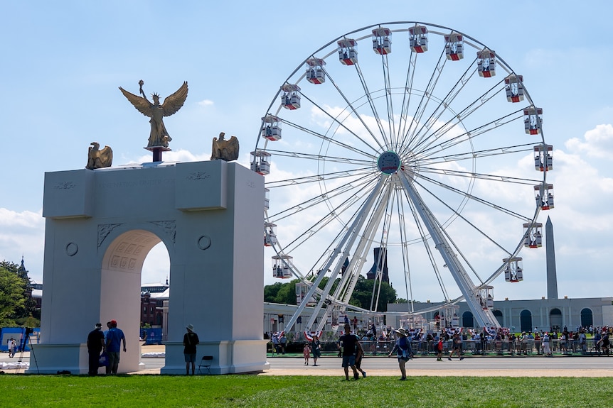 A Ferris Wheel and a large arch construction are seen on the National Mall in front of the Washington Monument.