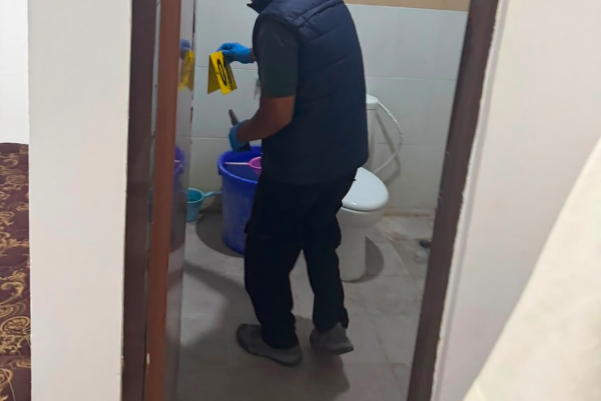 A man in a restroom wearing gloves placing a marker down