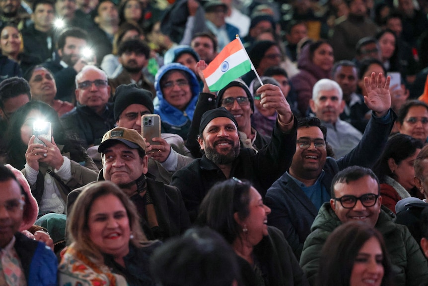 A large crowd waves Indian flags and takes photos.