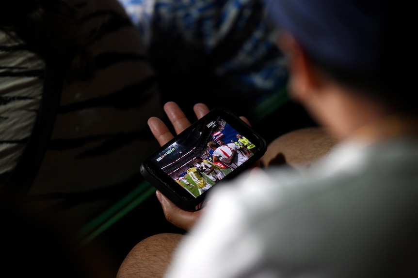 A man watches football on his phone.