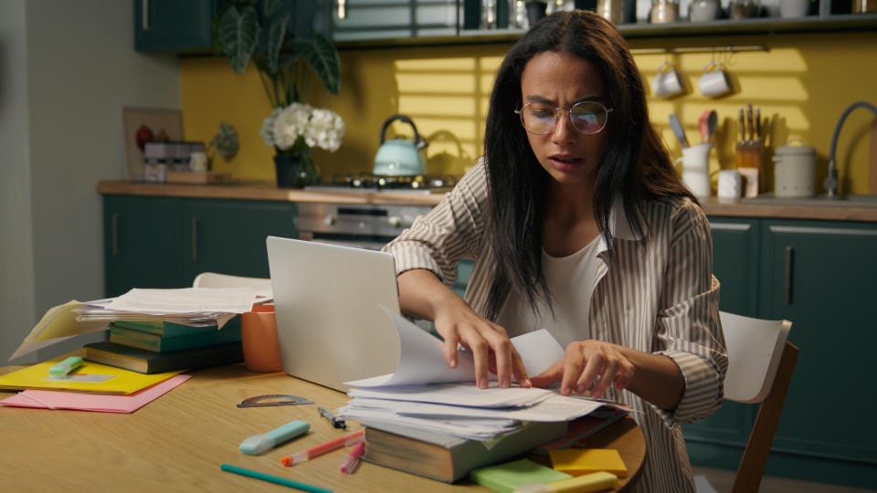 Stressed frustrated busy Latina Hispanic woman anxious businesswoman teen girl female high school student at home kitchen searching documents on table messy papers work laptop mistake problem stress