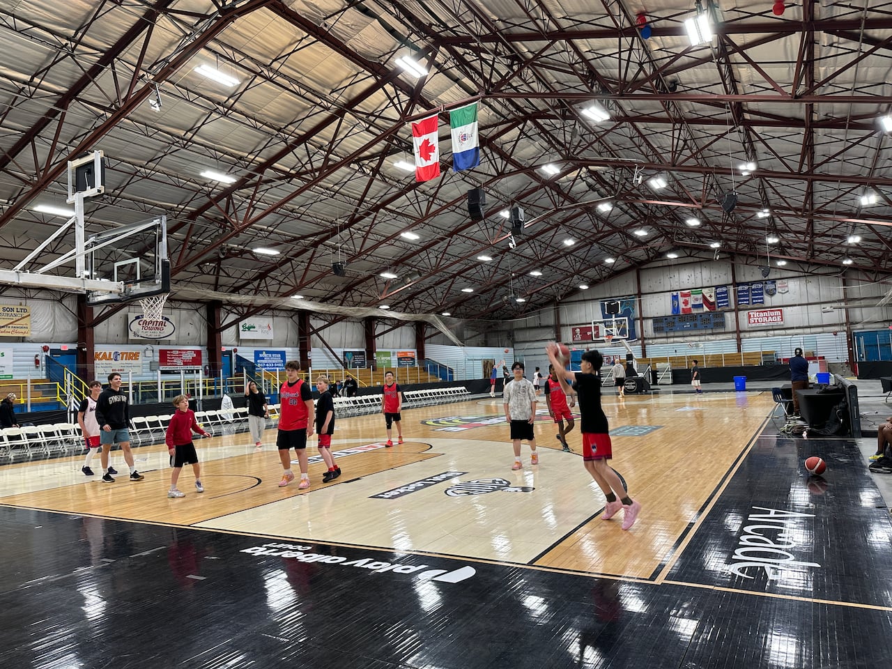 A small group of kids play a game of basketball on an indoor court as one of them jumps up to score.