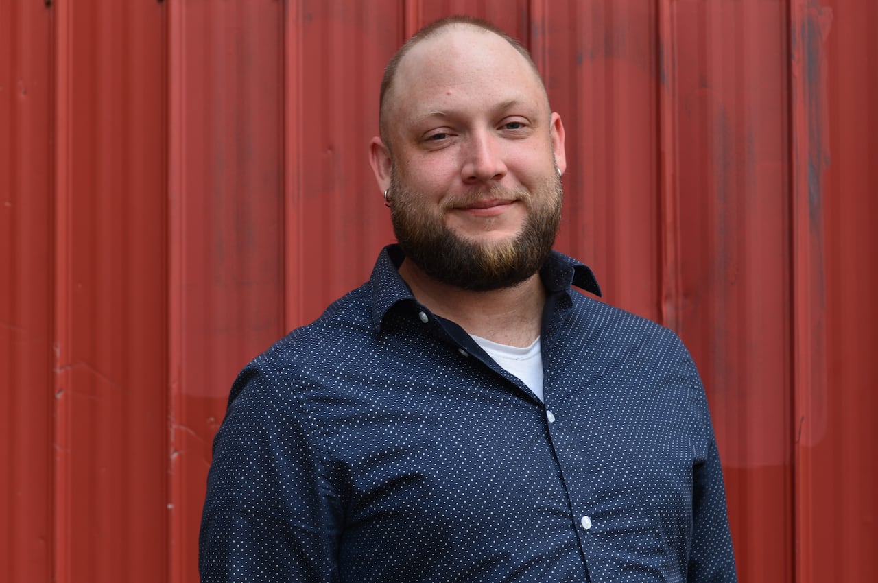 Scott Alan stands against a red background smiling at the camera.
