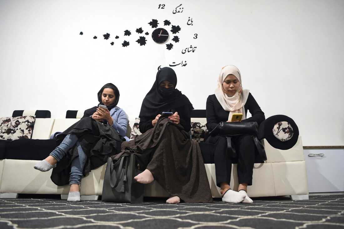 In this 2022 photo, three university students check their smartphones. In June, the Taliban announced a ban on the devices in certain sectors of society. The ripple effect is making students afraid to bring their smartphones to school.