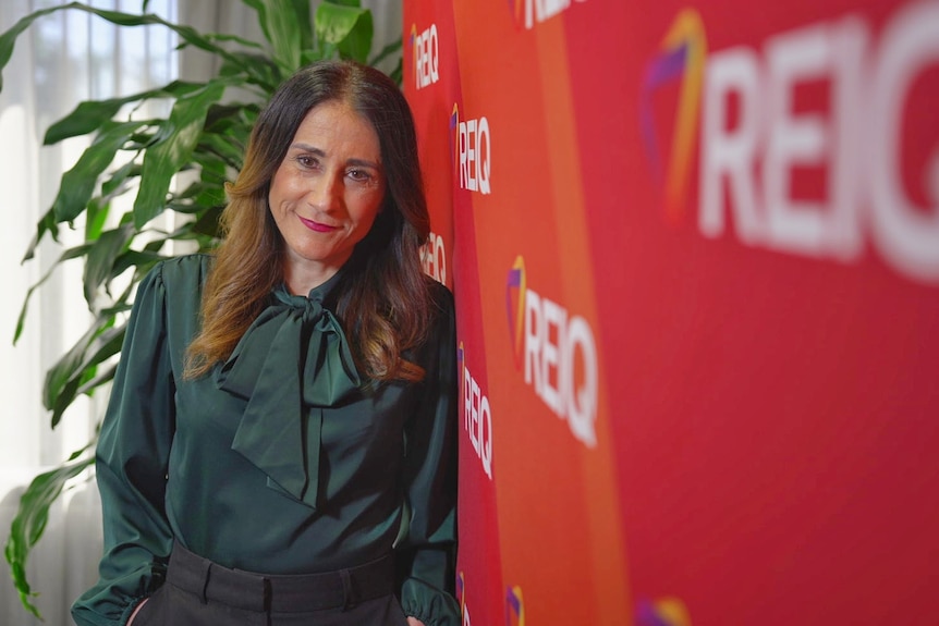 Antonia Mercorella smiles leaning against an orange sign for REIQ