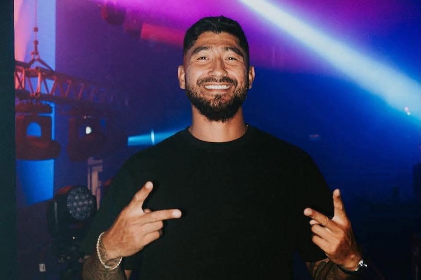 Josh Fawaz standing in a club setting throwing up two peace signs
