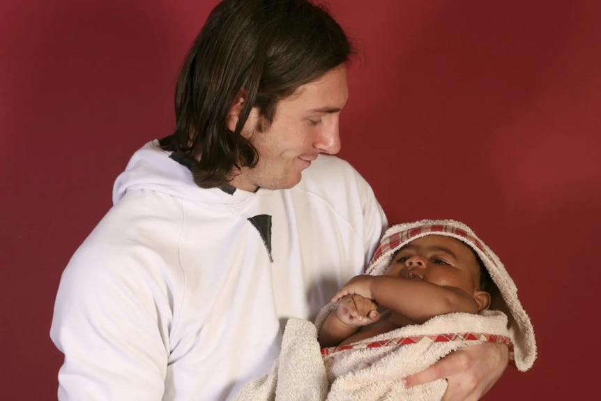 A man holds a baby in a towel.