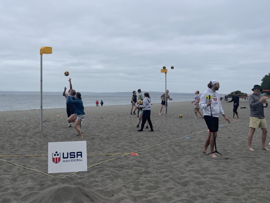 People jump up to get a korfball on a beach.