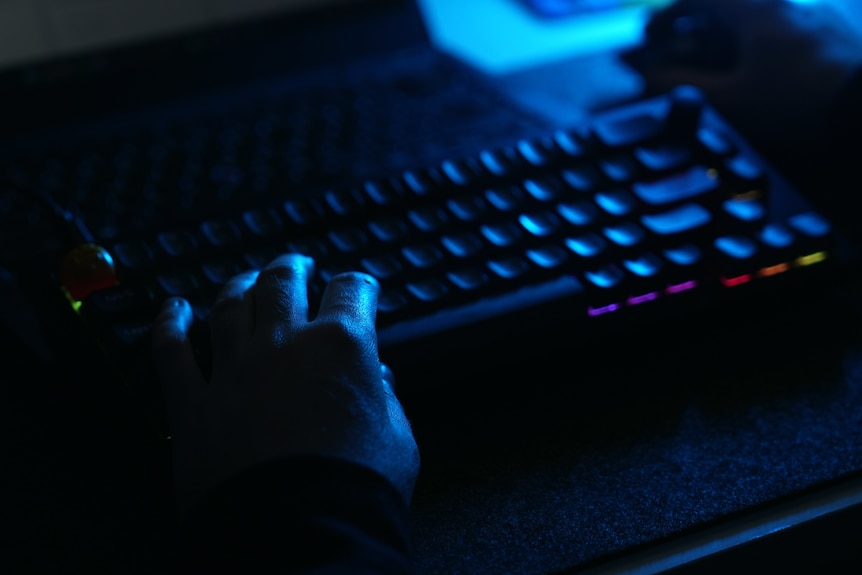 A close-up shot of a man's hands typing on a keyboard in a dark room.