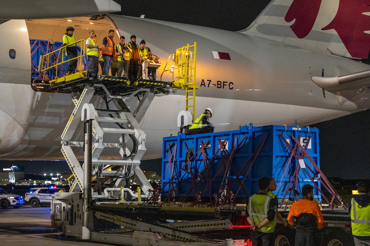 A blue container outside a large plane. People stand nearby on a scissor lift.