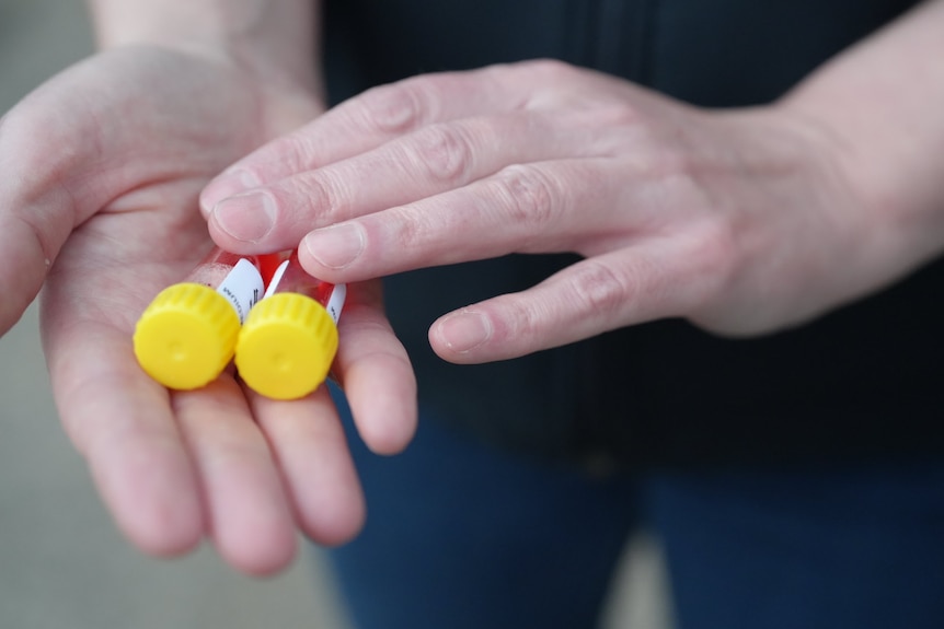 Two hands holding two canisters with yellow lids and red liquid