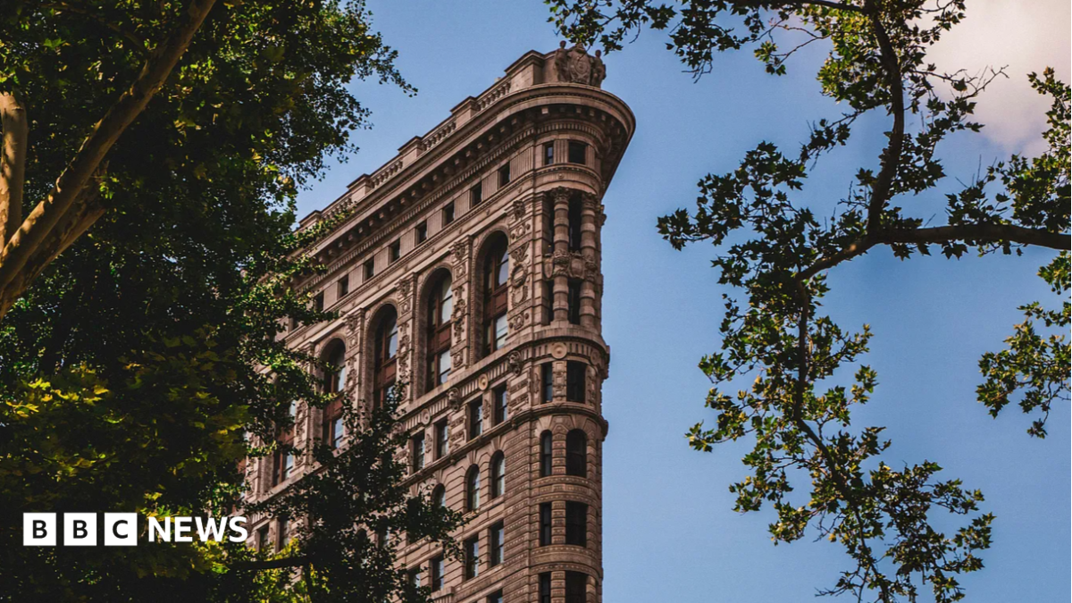 A view of the top section of the Flatiron Building, with trees surrounding it, showing its intricate Beaux-Arts detailing