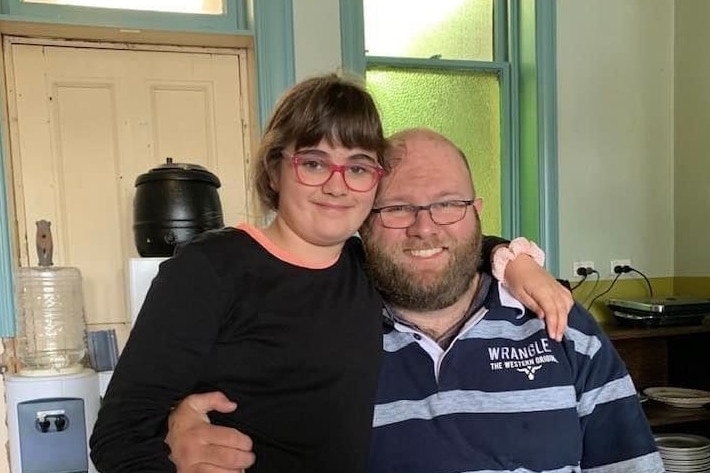 Girl wearing glasses puts her arm around her father at a kitchen table.