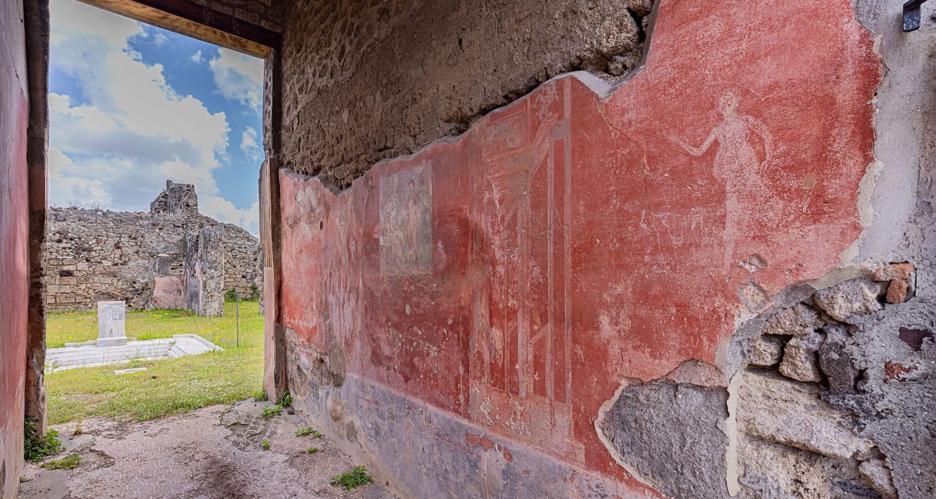 A view of ancient wall frescoes and ruins through an open doorway.