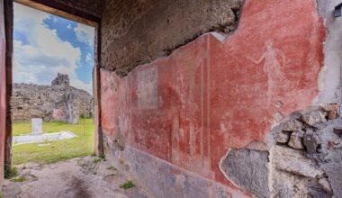 A view of ancient wall frescoes and ruins through an open doorway.