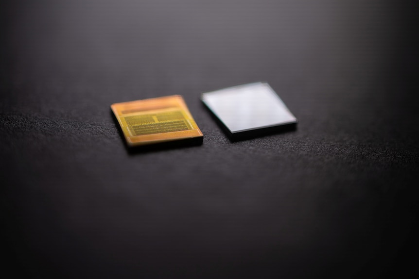 Two small square memory chips, one silver and the other gold in colour, on a black surface.