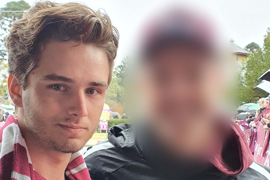 A young man poses for a photo with another man, who is blurred, at a rugby match.