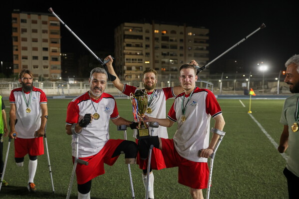Players from Damascus Governorate Club celebrate with the trophy after defeating Omayya Club in the final of Syria's first football tournament for people with disabilities at Al-Muhafaza Stadium in Damascus, Syria, Wednesday, July 29, 2026. (AP Photo/Ghaith Alsayed)