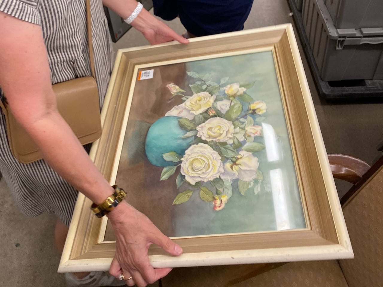 Outstretched hands hold a large framed realistic painting of a flower arrangement.