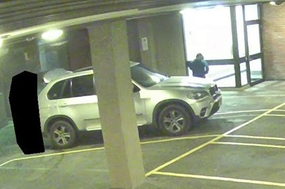 A woman and a person whose identity has been obscured near a car in car park area.