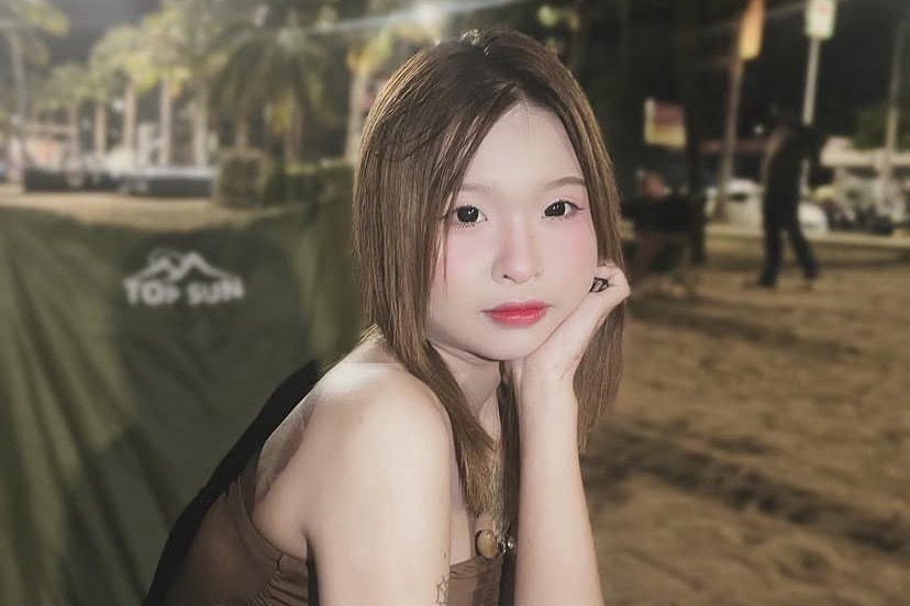 A young woman looks directly at the camera sitting on a bench.