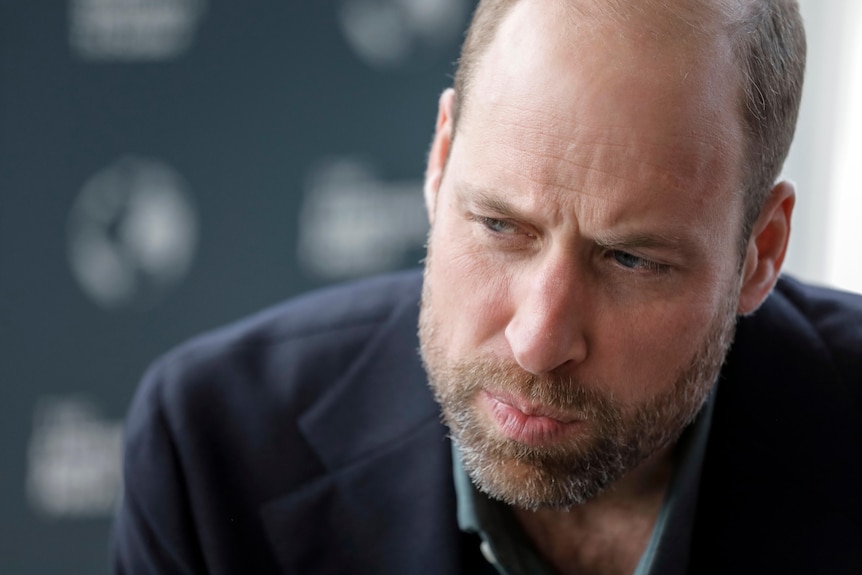 Prince William leans down with an overgrown beard and his lips pursed.