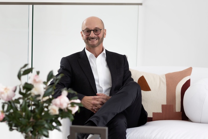 a man in a suit sits on a lounge smiling at the camera
