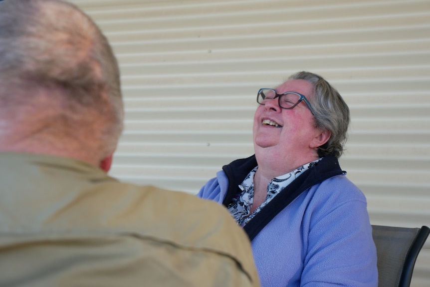A woman with short hair and glasses throws her head back laughing.