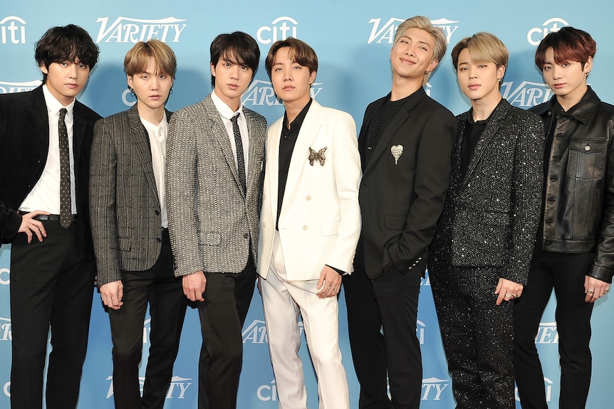 BTS band dressed in black, white and grey against a light blue background.