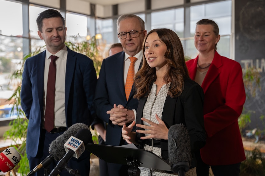 Jess Teesdale speaks at a press conference, with Dean Winter and Anthony Albanese standing behind her.