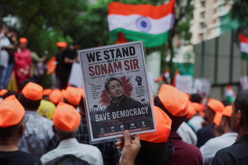 A poster showing Sonam Wangchuk is in focus in a crowd of protesters waving Indian flags
