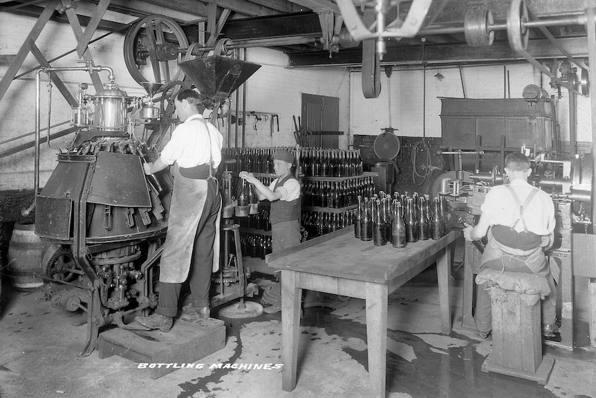 Three men working on old beer bottling machines