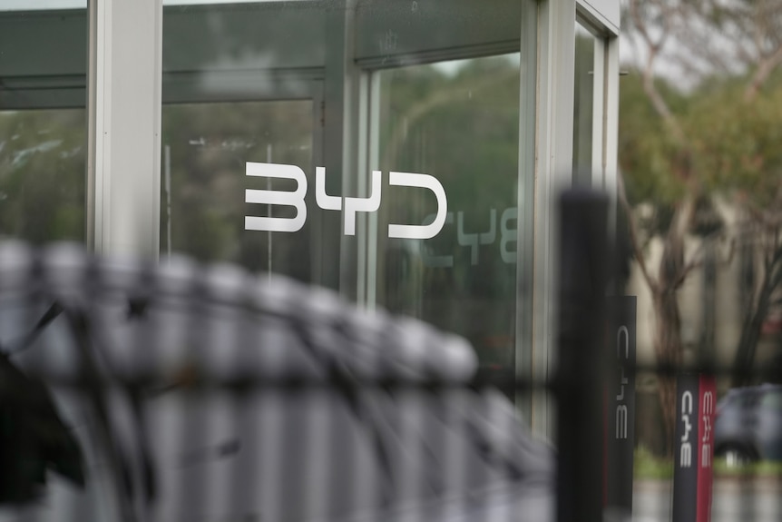Midshot of BYD sign on glass with a car in the foreground.