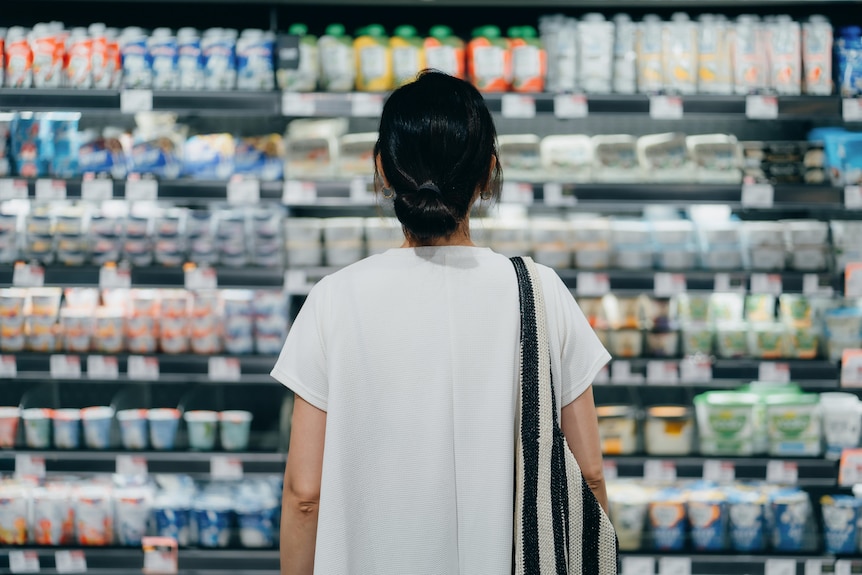 a young woman wearing a grey shirt looking at supermarket shelves