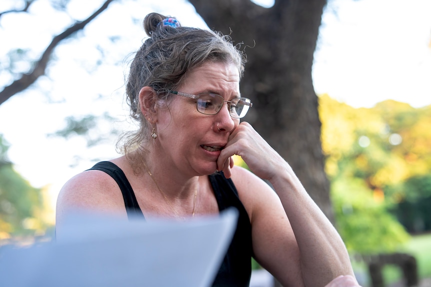 A close up shot of a white woman, with blonde / brown hair, with an upset expression, glasses on looking down.